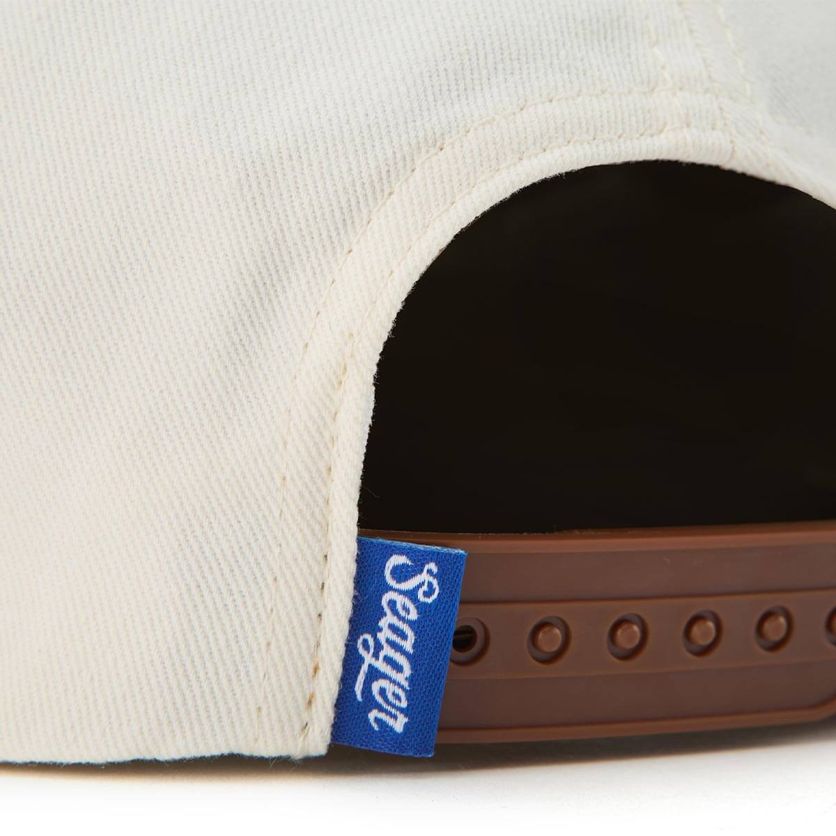 Close-up of a cap with a brown strap and blue 'Seager' logo on a white background