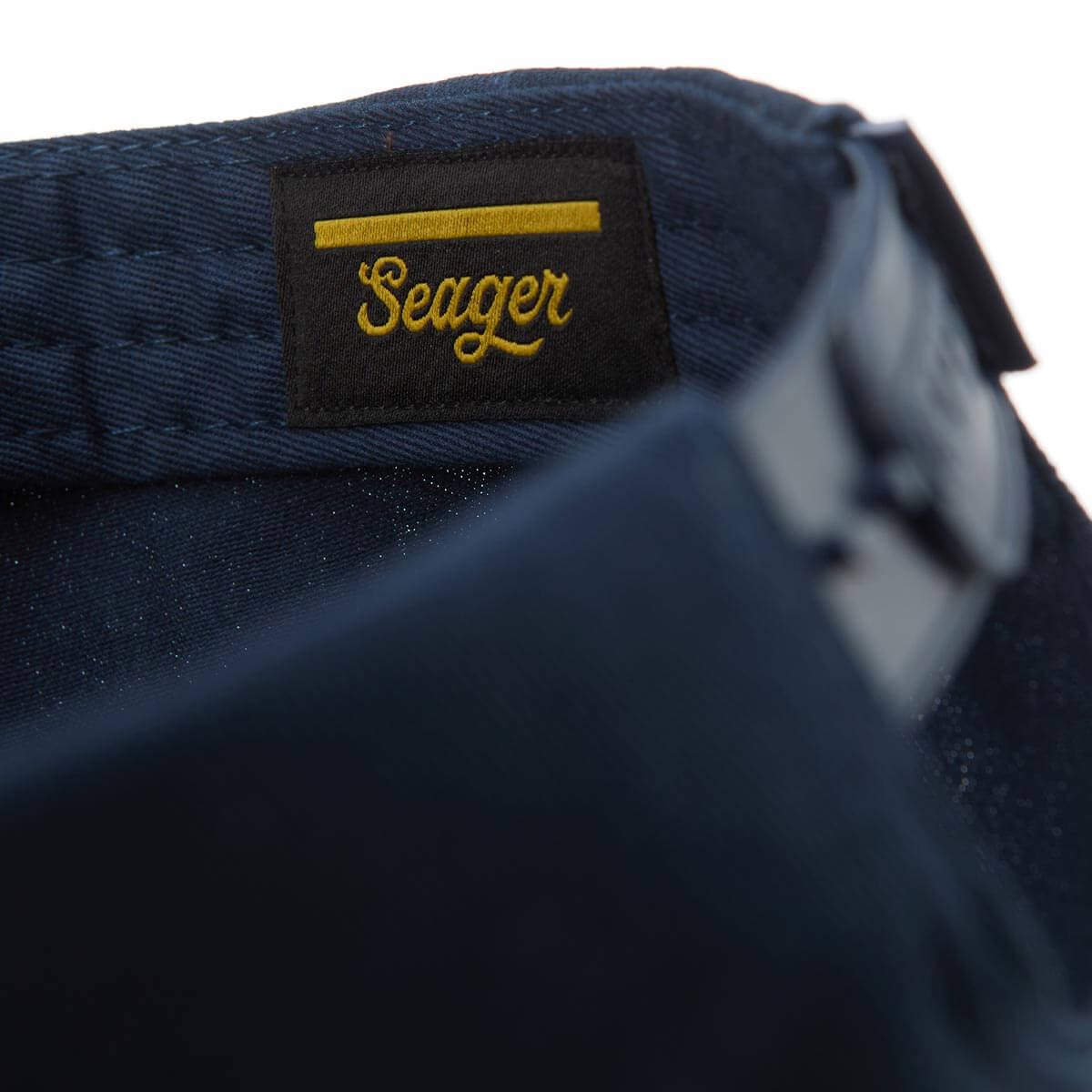 Close-up of a navy blue bag with a yellow 'Seager' logo on a white background