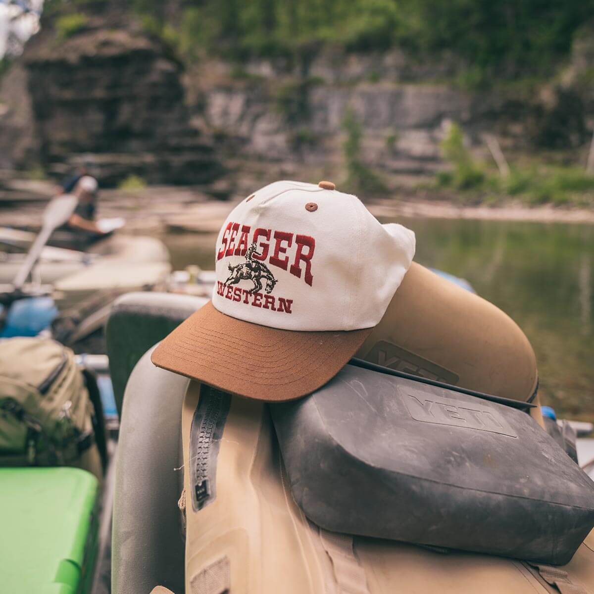 Seager cap on a boat with a scenic background of a lake and mountains.